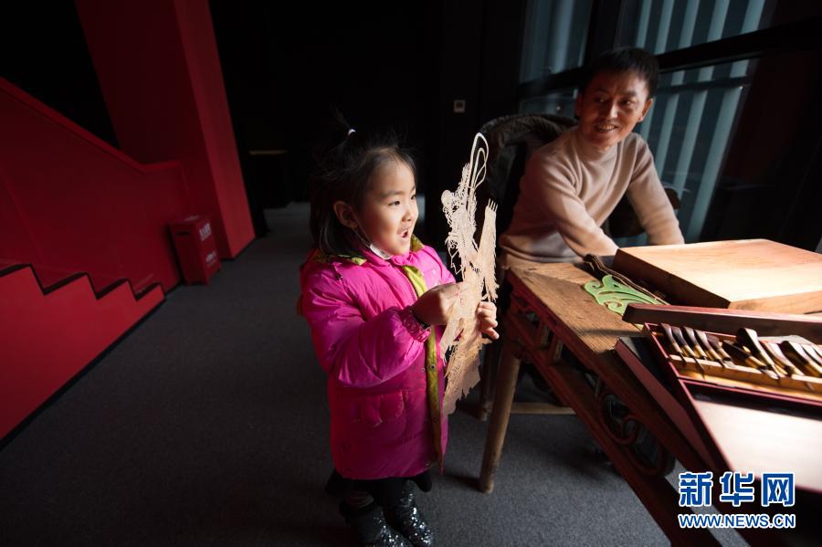 1月7日，在陕西西安明清皮影艺术博物馆，一名前来参观的小女孩拿起一幅先前雕刻好的皮影骨架。